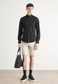 Black long-sleeve button-up shirt, beige shorts, black sneakers, and a black bag. The shirt has a collar and a fitted design.