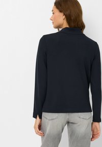 Marineblauw poloshirt met lange mouwen en een kraag, gemaakt van gladde stof, met zijsplitten aan de zoom, gecombineerd met lichtgrijze spijkerbroek.