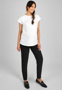 Maglietta bianca con maniche arrotolate, abbinata a pantaloni neri slim-fit. Il modello indossa mocassini neri, con una superficie di tessuto liscia.