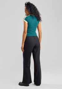 Teal-färgad enad t-shirt med gula detaljer, kombinerad med svarta utsvängda byxor. Strukturerad tyg, minimal design och inga synliga mönster.