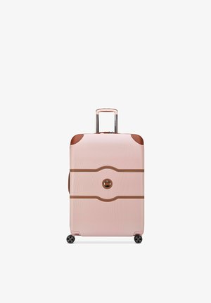 Valise rigide rose avec des accents en cuir marron, quatre roues et une poignée télescopique étendue, posée verticalement sur fond blanc.
