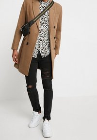 Cappotto di lana marrone con due bottoni frontali, abbinato a una camicia a stampa leopardata bianca e nera, jeans neri strappati e sneakers bianche.