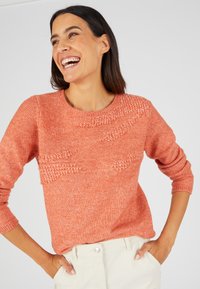 Pull en tricot corail avec des rayures diagonales texturées, col rond et manches trois-quarts, fabriqué à partir d'un tissu doux mélangé.