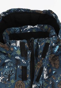 Lapsen sinisen takin kaulus, jossa on vetoketju ja tarrakiinnitys, ja jossa on metsän eläinten ja puiden kuvio ruskeana, valkoisena, vihreänä ja sinisenä.