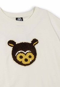 Camiseta de algodón en color blanco roto con un parche texturizado de la cara de un oso en marrón y amarillo, que presenta un detalle en forma de gota debajo del ojo derecho.
