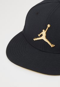 Cappellino da baseball nero con design strutturato, caratterizzato da un logo Jumpman ricamato in oro sulla parte anteriore e una visiera texturizzata.