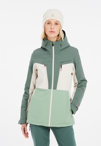 Zeleno-krémová softshell bunda s kapucňou, dvoma prednými vreckami na zips, textúrovanou tkaninou a kontrastnými farebnými blokmi.