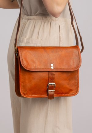 Bolso cruzado de cuero marrón con cierre de solapa, hebilla decorativa y acentos metálicos. Textura suave y forma rectangular.