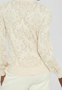 Ljusbeige tröja med en intrikat blommönster i damask, strukturerad stickad yta och ribbade ärmslut och fåll. Mjuk och åtsittande design.