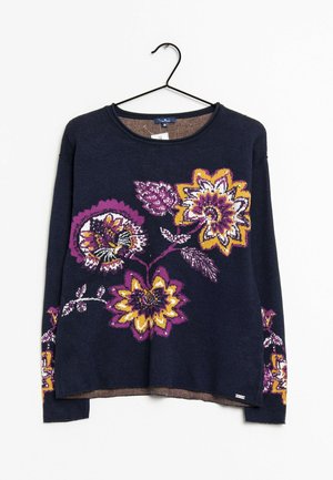 Marineblå langærmet sweater med store lilla, gule og hvide blomsterprint på fronten og ærmerne, hængende på en sort bøjle.