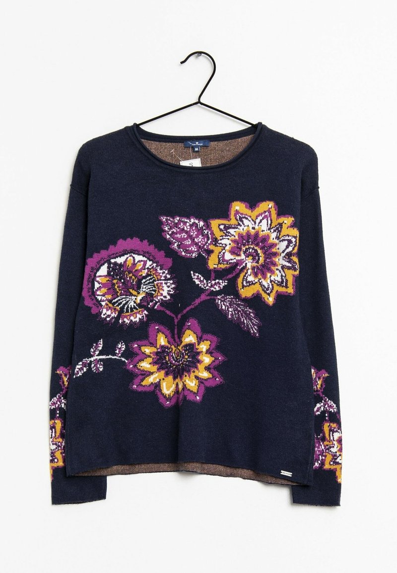 Pull bleu marine à manches longues avec de grands motifs floraux violets, jaunes et blancs sur le devant et les manches, accroché à un cintre noir.