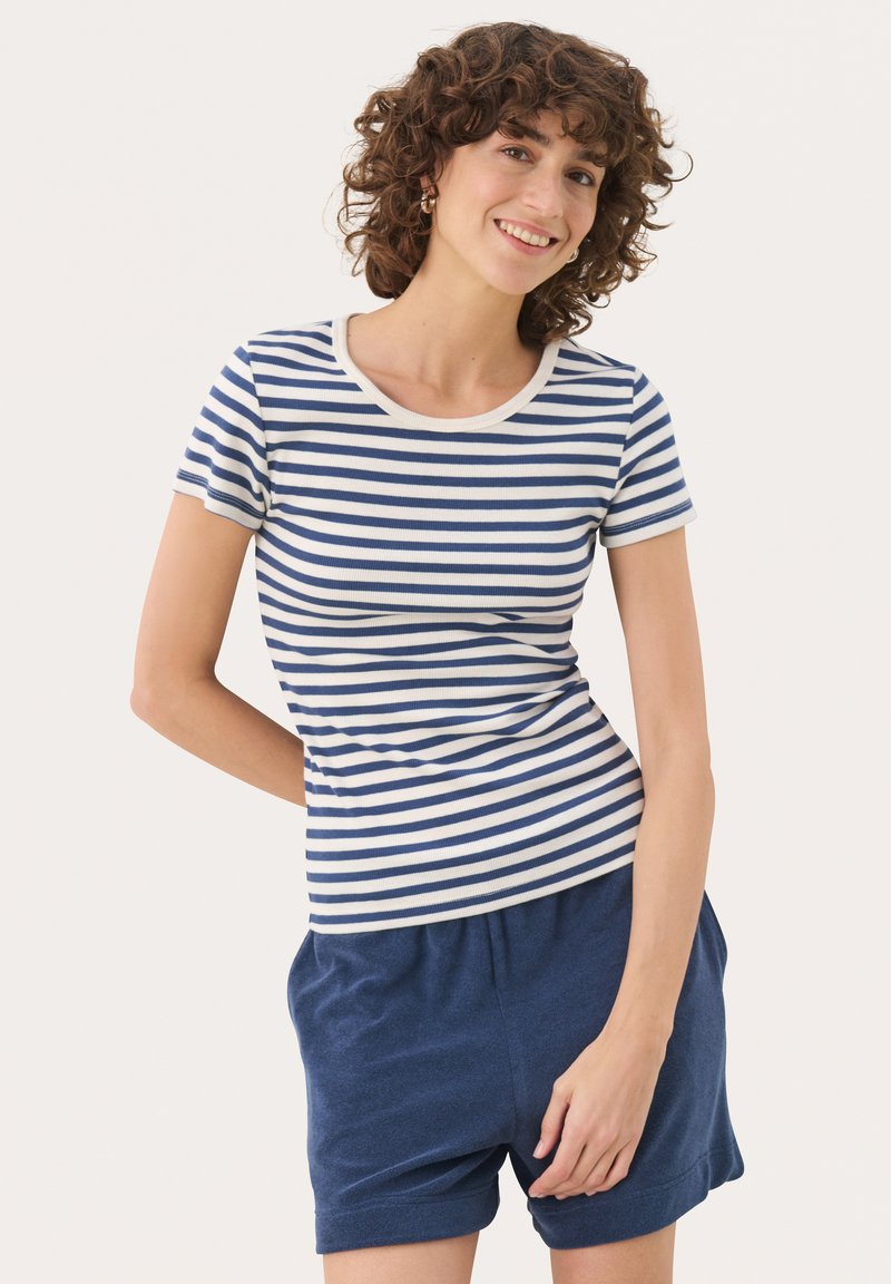 T-shirt rayé avec un col rond, présentant des rayures horizontales bleues et blanches, des manches courtes et une coupe ajustée. Associé à un short sombre.