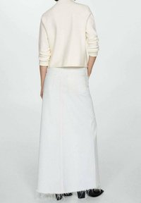 Jupe maxi en denim blanc avec ourlet effiloché et deux poches arrière, associée à un pull court beige clair. Design simple et minimaliste.