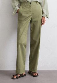 High-waisted straight-leg pants in olive green cotton, featuring front pockets and a button closure, worn with brown sandals.