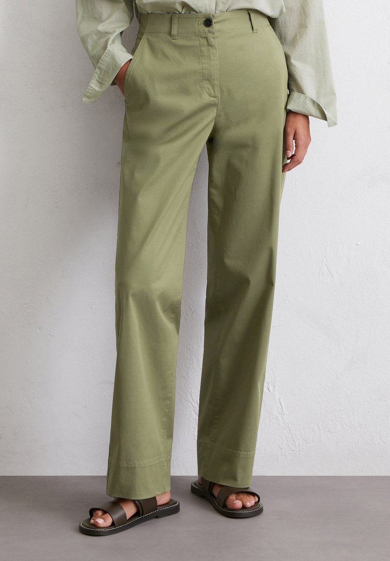 High-waisted straight-leg pants in olive green cotton, featuring front pockets and a button closure, worn with brown sandals.
