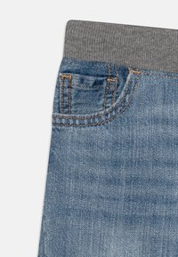 Pantaloni in denim azzurro chiaro con un elastico grigio in vita e cuciture arancioni, caratterizzati da un piccolo dettaglio di tasca frontale.