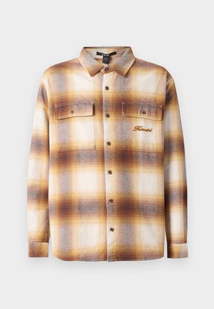 Brun och krämrutigt skjorta med knappar framtill, två bröstfickor och broderad logotyp på vänster sida. Gjord av ett strukturerat tyg.