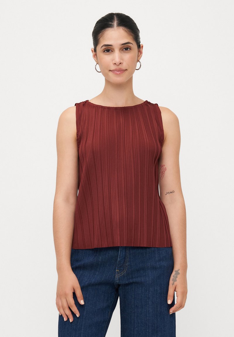 Top sans manches bourgogne avec des plis verticaux, encolure ronde et détails froncés aux épaules, associé à un pantalon en denim foncé.
