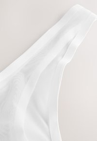 White mesh thong with a smooth waistband, featuring a sheer texture and a minimalist design. Lightly patterned fabric adds subtle detail.