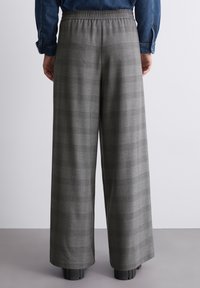 Gråternet, bukser med bred benlængde og elastisk talje. Stoffet har en blød tekstur og et subtilt ternet mønster. Fodtøj er ikke synligt.
