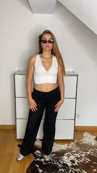 Vit kortärmad linne med djup V-ringning, parat med svarta vida byxor och metalliska silverfärgade skor. Accessoarer inkluderar svarta solglasögon.