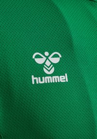 Grøn meshstof med en tekstureret overflade, der har et hvidt logo og designelementer, der ligner en bi. Mærket med brandnavnet "hummel."