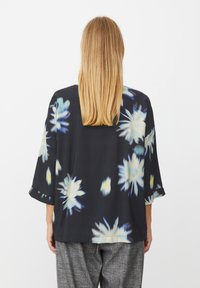 Sort blomstret bluse med løs pasform, der har store abstrakte blomster i hvid og blå. Indeholder trekvartærmer og blød stoftekstur.
