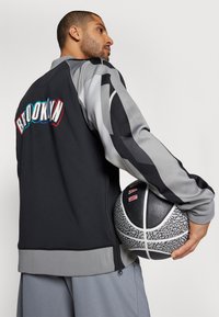 Black and gray athletic jacket with "BROOKLYN" in colorful letters on the back, paired with a textured black and gray basketball.