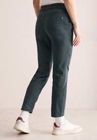 Mörkgröna joggers med elastisk midja, med bakfickor och tapered bendesign, kombinerat med vita sneakers och ribbade strumpor.