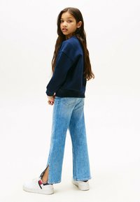Sudadera navy, corte relajado, de manga larga. Jeans de pata ancha azul claro con aberturas laterales, combinados con zapatillas blancas con acentos en navy y rojo.