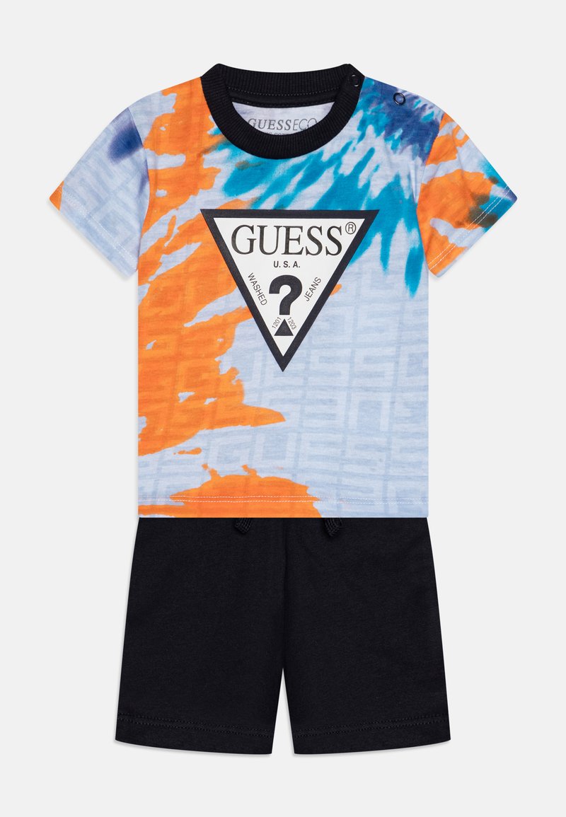 Tricou cu un model tie-dye multicolor în nuanțe de portocaliu, albastru și albastru deschis, având un triunghi-logo negru; asociat cu pantaloni scurți negri.