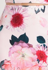 Tela con estampado floral en un suave tono de rosa, que presenta una mezcla de grandes peonías rosas y girasoles rojos, con hojas verdes y una textura suave.