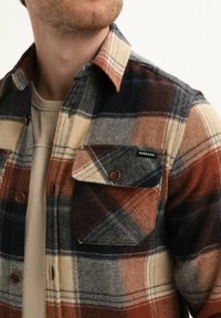 Bruin, marineblauw en roomkleurig geruite flanellen shirt met een knoopsluiting op de borst en een merklabel, met een klassieke kraag en een zachte textuur.
