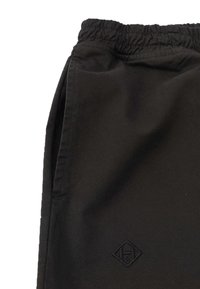 Schwarze Hose mit elastischem Bund, seitlichen Taschen und einem kleinen geprägten Logo. Glattes Gewebe mit matter Oberfläche und taillierter Passform.