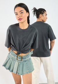 Dark gray cotton t-shirt knotted at the waist, paired with a light blue denim mini skirt featuring pleats and a large belt buckle.
