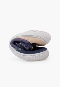 Baskets flexibles pliées en deux, montrant une semelle en caoutchouc blanche, une tige en tissu beige et bleu, mettant en avant leur design pliable.