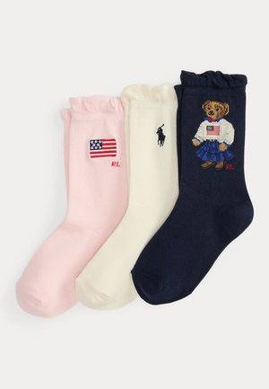 Trzy damskie skarpetki z falbanką u góry w kolorach różowym, kremowym i granatowym, każda z haftowanymi, amerykańskimi motywami i inicjałami logo Ralph Lauren.