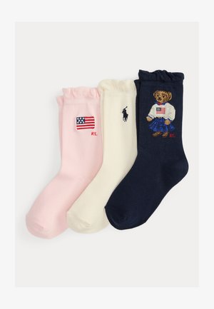 Trzy damskie skarpetki z falbanką u góry w kolorach różowym, kremowym i granatowym, każda z haftowanymi, amerykańskimi motywami i inicjałami logo Ralph Lauren.