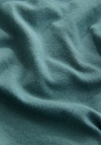 Tissu à texture douce de couleur sarcelle avec des plis légers et un éclairage subtil mettant en valeur le motif tricoté.