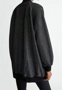 Giacca bomber nera con superficie testurizzata, dotata di colletto e polsini a costine. Silhouette oversize, con un design leggermente ampio.
