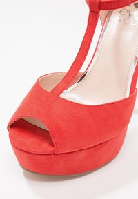 Sandale à plateforme en suède rouge avec bout ouvert et bride en T sur fond blanc.