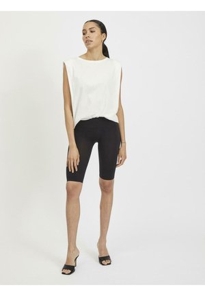 Weißes ärmelloses Oberteil mit entspannter Passform, kombiniert mit schwarzen Radlerhosen. Das Model trägt schwarze Sandalen; minimalistisch im Design, glatte Textur.