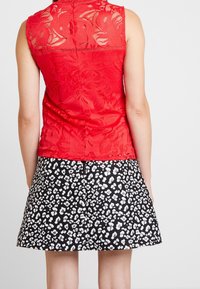 Top sin mangas de encaje rojo con patrón floral, combinado con una falda negra con manchas de leopardo blancas y un dobladillo recto.