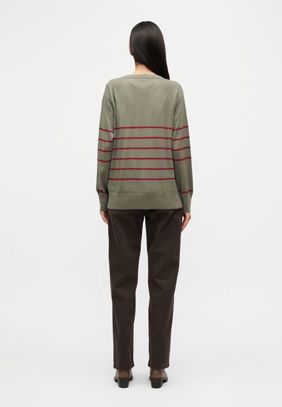 Μπλούζα μακρυμάνικη σε ελιά πράσινο με οριζόντιες μπορντό ρίγες. Μαλακό ύφασμα, άνετη εφαρμογή, ριμπ τελείωμα. Συνδυασμένη με σκούρο καφέ παντελόνι και παπούτσια με τακούνι.