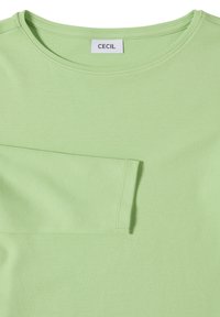 Camiseta de algodón verde claro con cuello redondo y un solo bolsillo parche. Textura suave, diseño sencillo y detalles sobrios.