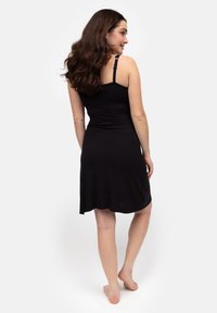 Czarna sukienka bez rękawów z dopasowanym gorsetem i rozkloszowanym dołem, wykonana z miękkiego materiału. Widok od tyłu ukazuje regulowane ramiączka i gładką teksturę.