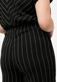 Pantalons noirs à rayures avec un tissu texturé, présentant de fines rayures verticales blanches, une taille élastique et une coupe décontractée.