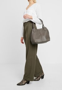 Šedá kožená taška přes rameno s dvojitými držadly, obdélníkového tvaru, hladké struktury, doplněná olivovými širokými kalhotami a vzorovanými kotníkovými botami.