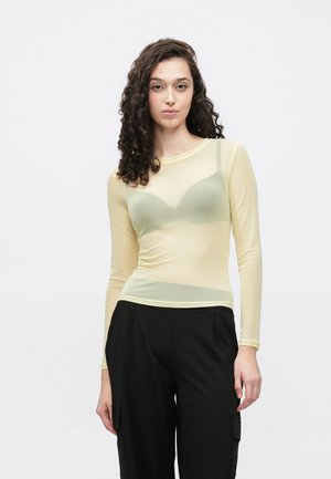 Gennemsigtig langærmet top i lys gul, med en tætsiddende pasform, rund halsudskæring og subtil teksturoverflade. Båret over en grøn bh.