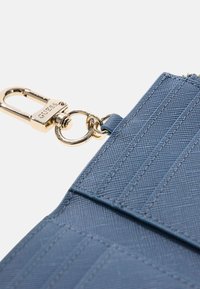 Borsa sintetica blu con linee verticali strutturate, ferrature dorate e un aggancio a clip. Dotata di un anello circolare per l'attacco di accessori.